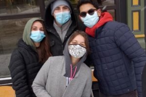 Four students standing together wearing masks, bundled up in winter clothes and scarves