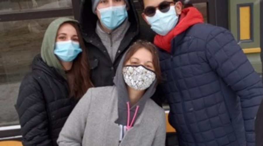 Four students standing together wearing masks, bundled up in winter clothes and scarves