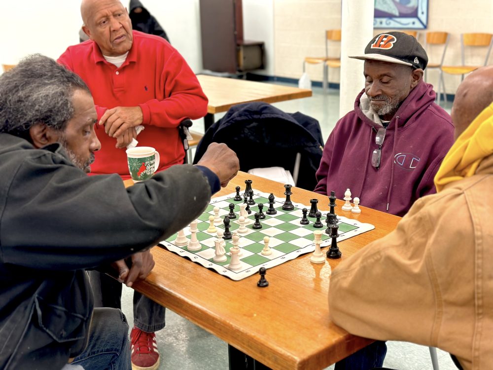 four older men sitting around a table, playing chess.
