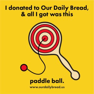 An illustration of a paddle ball with a target design in the center with a red ball on a string attached. The background color is yellow. Text above and below reads I donated to our daily bread and all I got was this paddle ball. www.ourdailybread.us